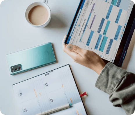 Hands holding a tablet beside a phone and planner