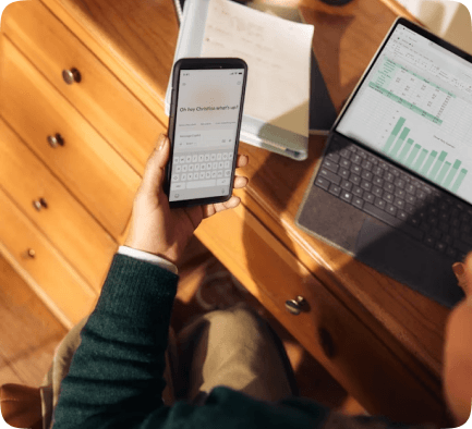 Person using a phone and tablet at a wooden desk
